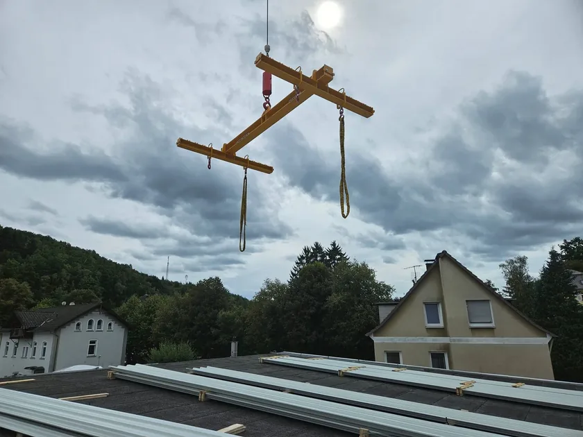 Gelbe Krantraverse mit Anschlagmitteln über dem Dach