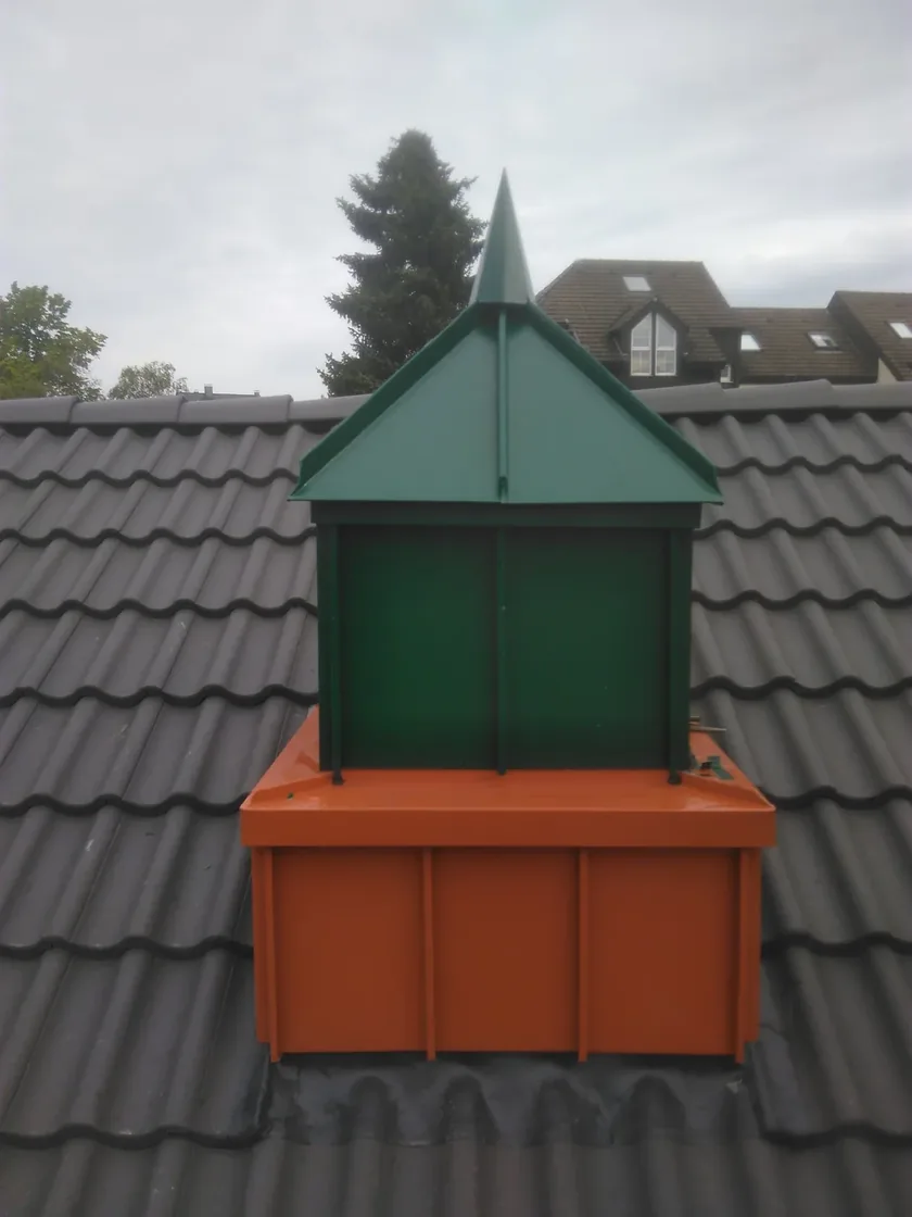 Grüner Schornsteinkopf mit Spitze auf orangefarbenem Sockel am Ziegeldach